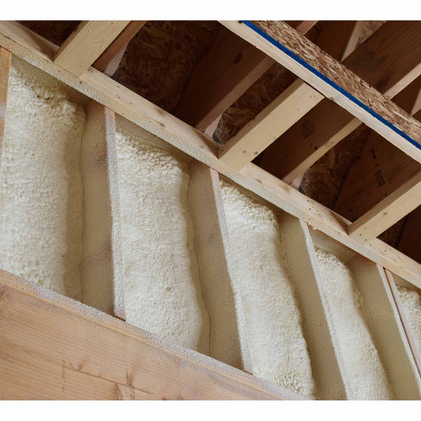 Cured off-white spray foam insulation filled between vertical wooden wall studs and ceiling roof rafters in building framing.