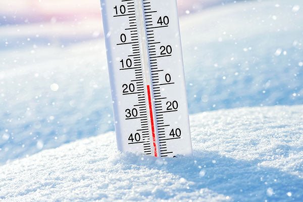 Glass outdoor thermometer displaying freezing temperatures stuck in a bank of fresh snow during a snowfall.